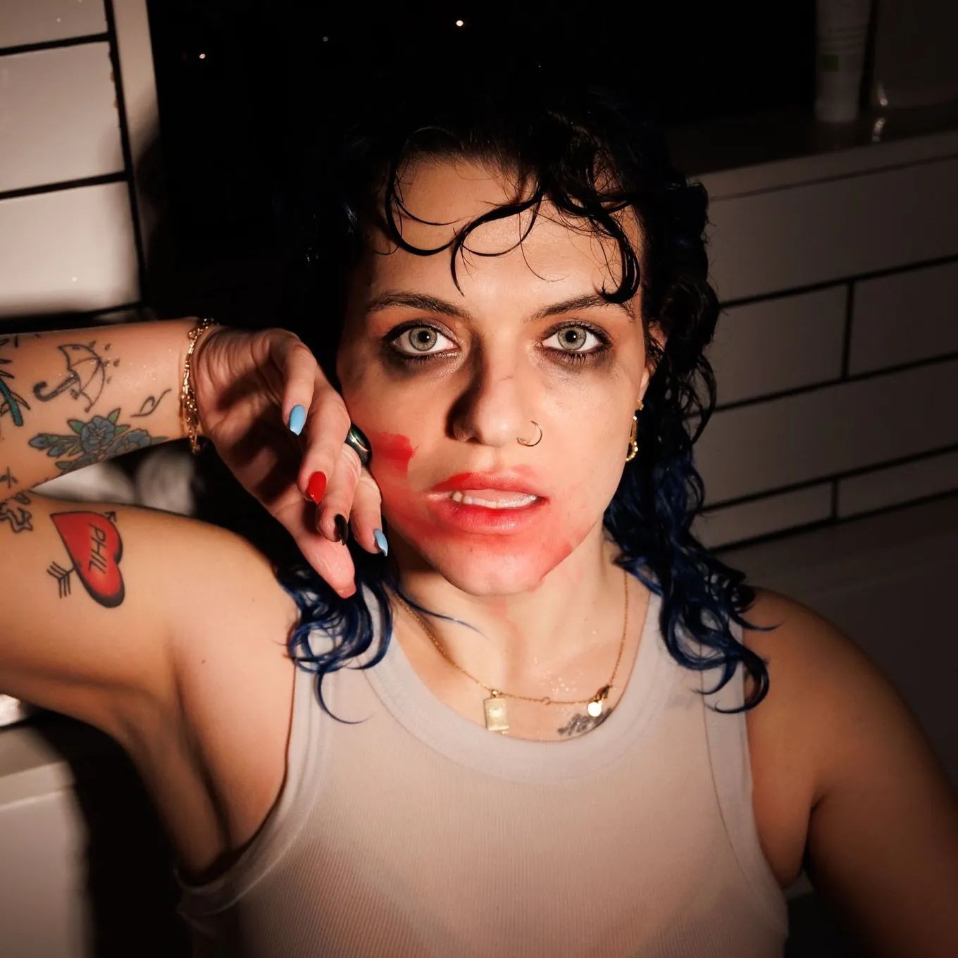 Alex Ray in a white vest, dark curls with blue-dyed ends and red make-up smeared across one cheek, taped up like a polaroid