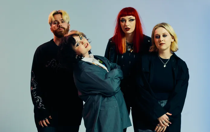 The four of them grouped against a pale blue backdrop, one with bright red hair