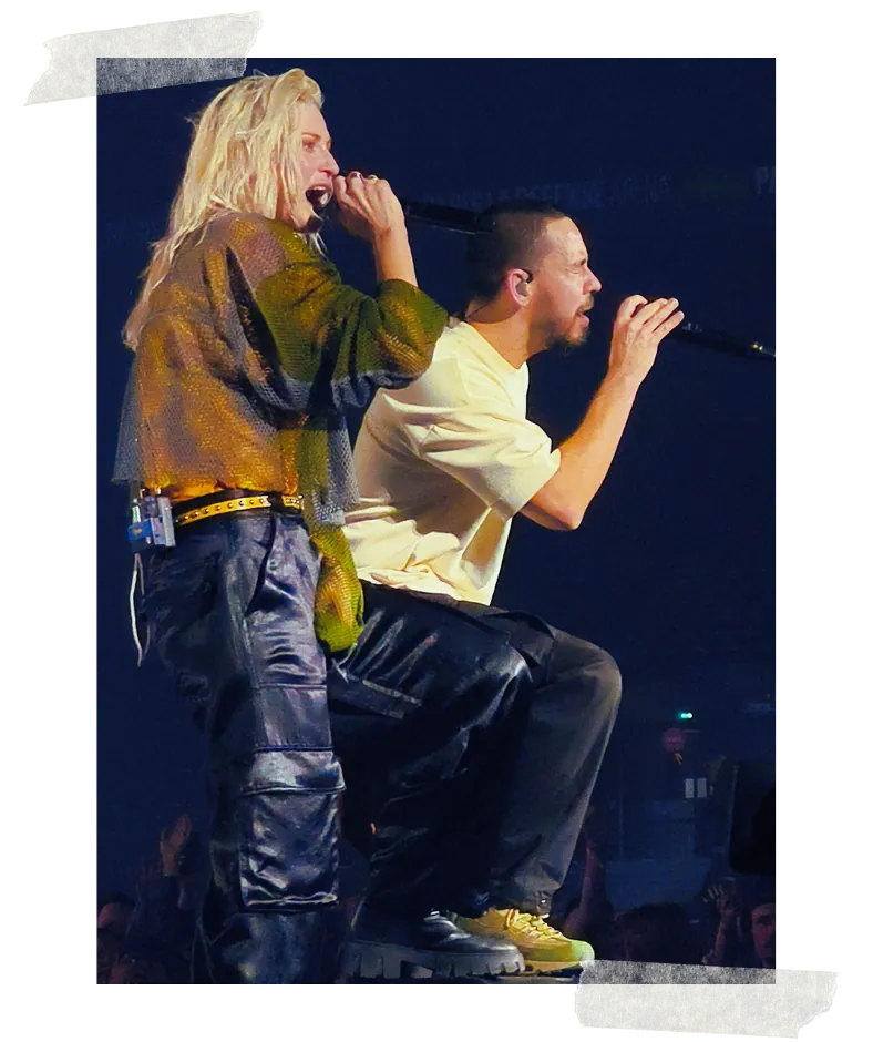 The two vocalists side by side on a riser, both into their microphones