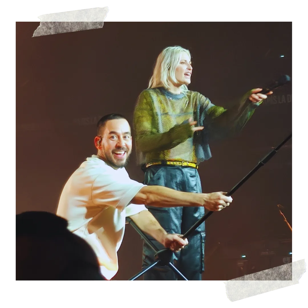 The two vocalists laughing, one holding a selfie stick out over the crowd