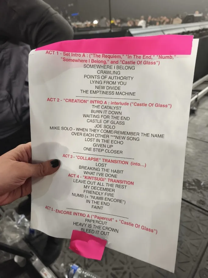 A hand holding the printed setlist, five acts of song titles annotated in pink