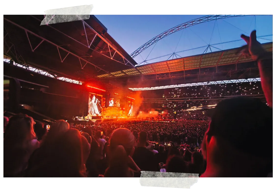 The stadium at night seen from the stands, the arch above and the stage burning orange below