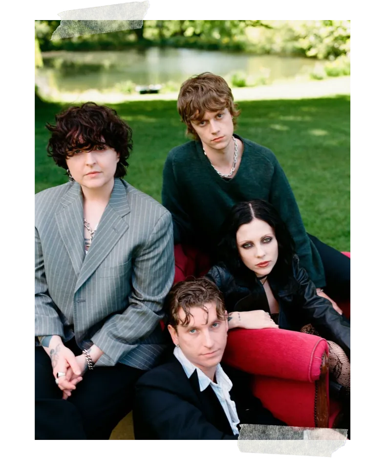 The band grouped around a red chaise longue on a lawn, a lake behind