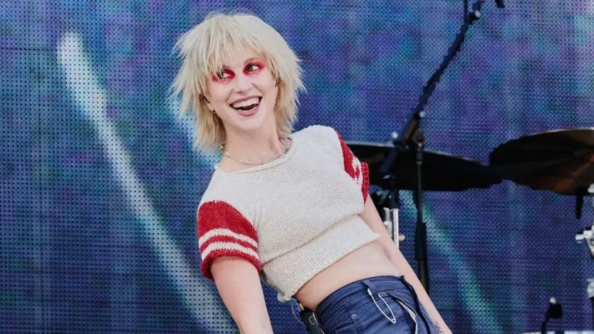 The singer laughing in close-up against a pixelated screen backdrop