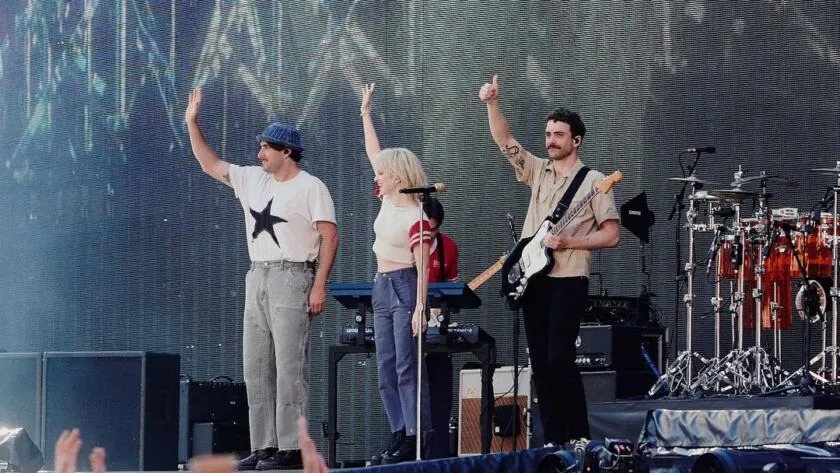 Three of the band taking a bow with their arms raised