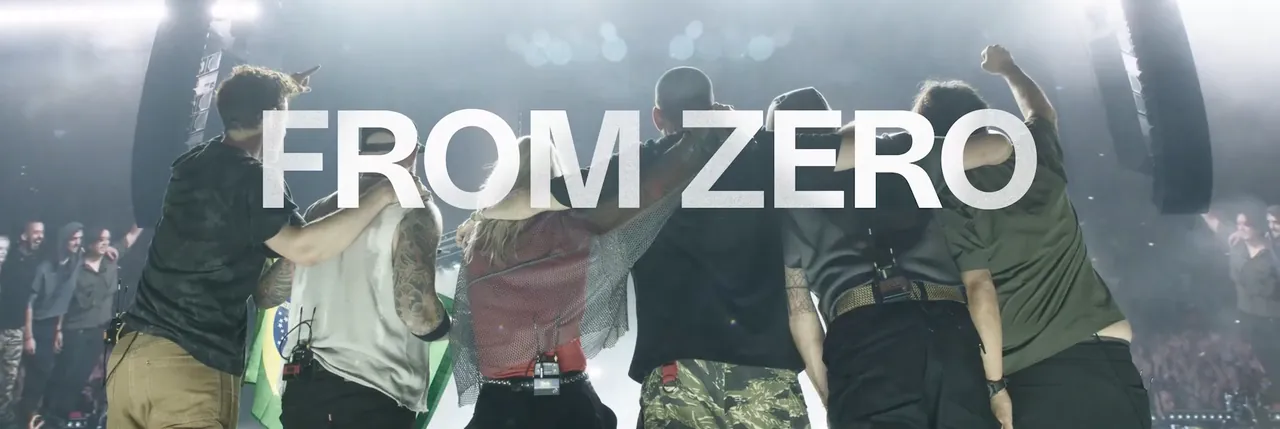 The band seen from behind on the São Paulo stage, arms raised to a full stadium, the words FROM ZERO across the screen