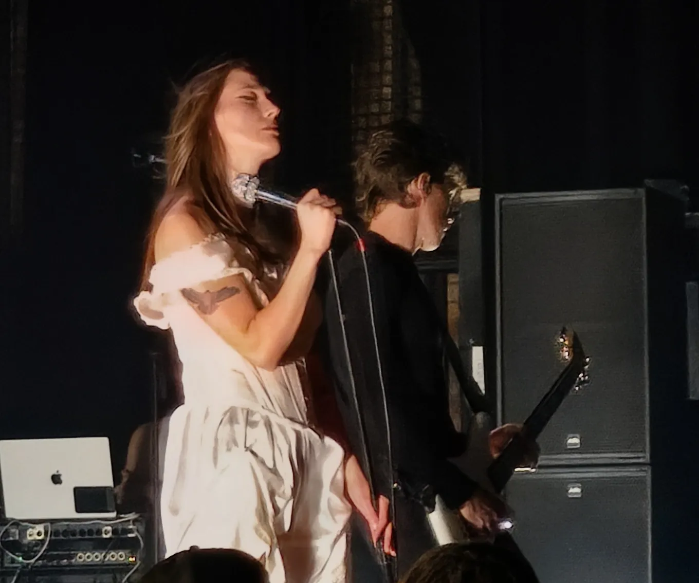 Theresa Jarvis in a white dress, eyes closed, both hands on the microphone, the guitarist behind her